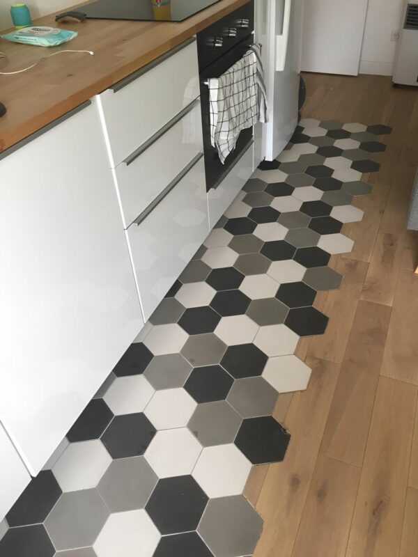 Revêtement de cuisine en parquet et carreaux de ciment hexagonaux noirs, blanc et gris.